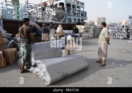 Eine Gruppe von asiatischen Hafenarbeiter (abgeänderter Wortlaut) Vorbereitung von für die Ausfuhr bestimmten Waren auf einem Verankerten Dhow (arabischen Boot an der Uferstraße des Dubai Creek in D geladen werden Stockfoto