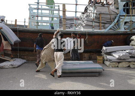 Eine Gruppe von asiatischen Hafenarbeiter (abgeänderter Wortlaut) Vorbereitung von für die Ausfuhr bestimmten Waren auf einem Verankerten Dhow (arabischen Boot an der Uferstraße des Dubai Creek in D geladen werden Stockfoto