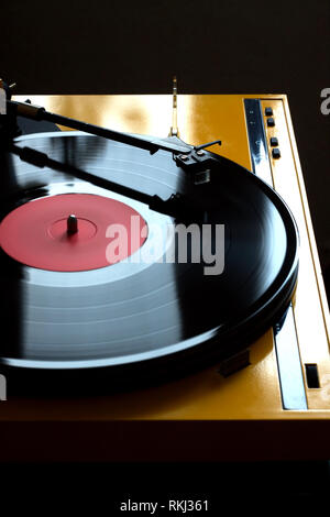 Spieler in gelb Anästhesieprotokoll mit schwarzen Tonarm mit Rotation Schallplatte mit Red Label auf dunklem Hintergrund. Vertikale Foto Seite Ansicht schließen Stockfoto