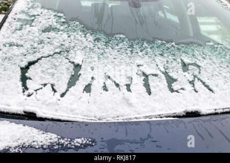 Auto Windschutzscheibe mit Schnee und das Wort Winter im Schnee oberhalb der Scheibenwischer geschrieben. Stockfoto