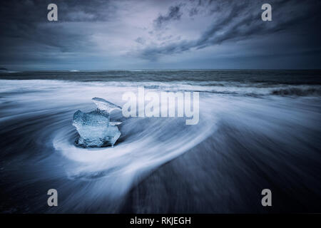 Meer driftet in um die Eisberge und das Gletschereis, die am Strand auf dem schwarzen Sand am Gletschersee Jökulsárlón, Island gefegt wird Stockfoto