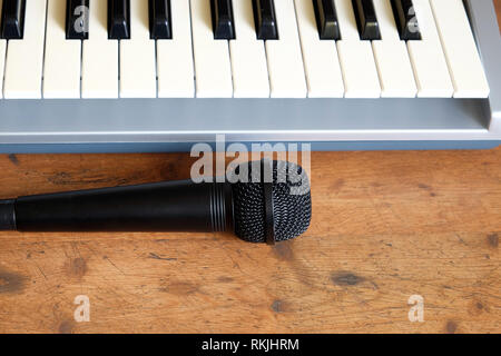 Schwarze stimme Mikrofon und Elektronische Synthesizer Keyboard in Silber Kunststoffgehäuse mit schwarzen und weißen Tasten auf hölzernen Hintergrund Vorderansicht closeup Stockfoto