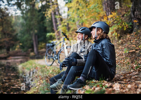 Ein älteres Paar mit elektrobikes sitzen draußen im Park im Herbst, ruhen. Stockfoto