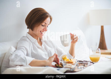 Eine Frau mit Frühstück im Bett am Morgen. Stockfoto