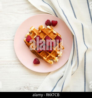 Ansicht von oben, traditionelle belgische Waffeln mit Himbeeren auf Rosa die Platte über der weißen Holz- Oberfläche. Overhead, von oben. Stockfoto
