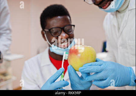 Gesunde Zähne sind der Schlüssel zum Glück! African American männlicher Arzt in der zahnmedizinischen Klinik mit einem Apple und Zahnbürste in die Hände. Stockfoto