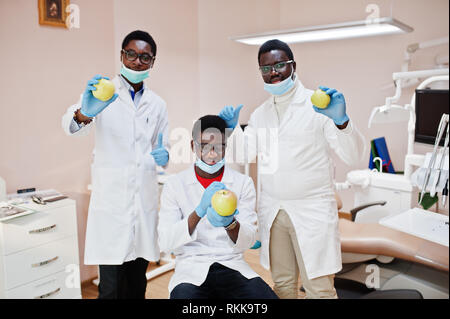 Gesunde Zähne sind der Schlüssel zum Glück! Drei afrikanischen amerikanischen männlichen Ärzten und Kollegen in der zahnmedizinischen Klinik mit einem Apfel in der Hand. Stockfoto