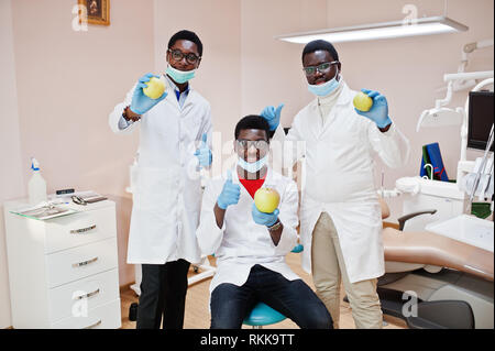 Gesunde Zähne sind der Schlüssel zum Glück! Drei afrikanischen amerikanischen männlichen Ärzten und Kollegen in der zahnmedizinischen Klinik mit einem Apfel in der Hand. Stockfoto