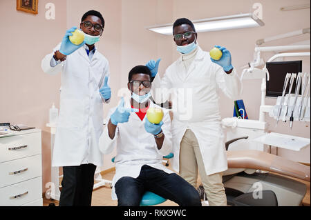 Gesunde Zähne sind der Schlüssel zum Glück! Drei afrikanischen amerikanischen männlichen Ärzten und Kollegen in der zahnmedizinischen Klinik mit einem Apfel in der Hand. Stockfoto