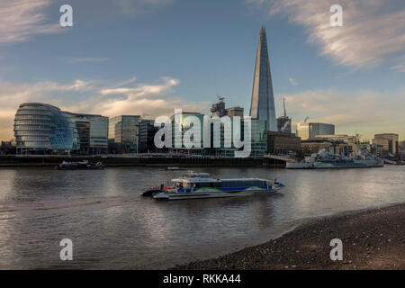 Am Flussufer in der Nähe der Themse in London. Morgen mit Sonne auf der Gebäude wider. Boot den Fluss übergeben. Stockfoto