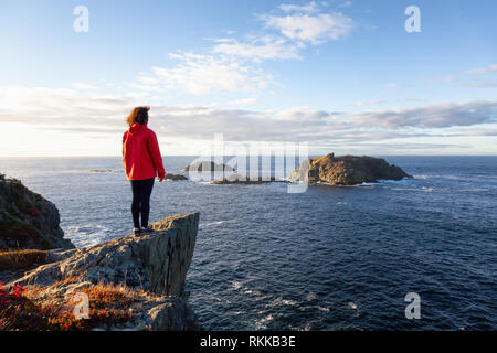 Frau in der roten Jacke steht am Rand einer Klippe und genießen das wunderschöne Meer Landschaft. Im Crow Head, North Twillingate Insel, Newfoun genommen Stockfoto