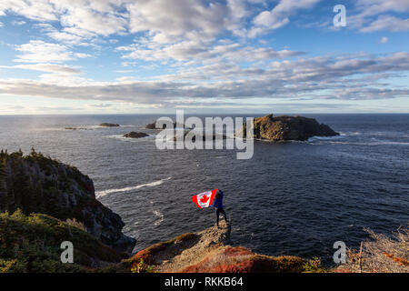 Abenteuerliche Frau mit einem kanadischen Flagge auf einem felsigen Atlantik Küste an einem sonnigen Tag. In sleepy Cove, Krähe Kopf, Twillingate, Newfoundla genommen Stockfoto