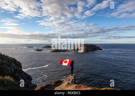 Abenteuerliche Frau mit einem kanadischen Flagge auf einem felsigen Atlantik Küste an einem sonnigen Tag. In sleepy Cove, Krähe Kopf, Twillingate, Newfoundla genommen Stockfoto