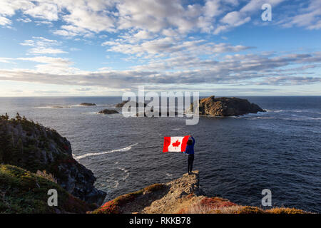Abenteuerliche Frau mit einem kanadischen Flagge auf einem felsigen Atlantik Küste an einem sonnigen Tag. In sleepy Cove, Krähe Kopf, Twillingate, Newfoundla genommen Stockfoto