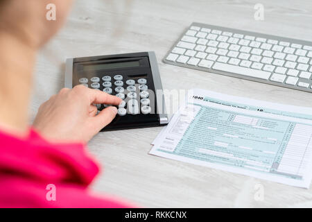 Über der Schulter Foto von Frau Berechnung der US-Steuer Formular neben Computer Tastatur und Steuerformular 1040. Stockfoto