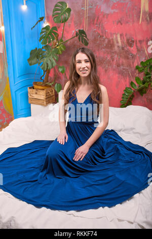 Portrait einer jungen Brünette Dame, trägt blaue Kleid. Das Girl posiert, blickte nach unten. Green Palm Blätter im Hintergrund. Stockfoto