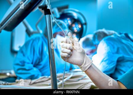 Dropper in eine Vene in der Nähe - auf dem Hintergrund der Chirurgischen funktionsfähig. Arzt Frau in sterile Handschuhe Vorbereitung eines Patienten für die Chirurgie. Stockfoto