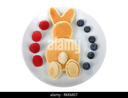 Pfannkuchen in einer Bunny rabbit Muster, Banane für Schwanz und Füße, frisch Himbeeren und Blaubeeren auf der Platte. Auf weissem Hintergrund. Stockfoto