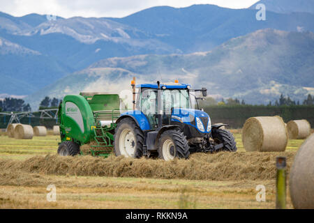 Annat, Canterbury, Neuseeland - 1. Februar 2019: ein Traktor und Ballenpresse Heu Arbeiten auf einer Farm an einem heißen Tag im Sommer Stockfoto