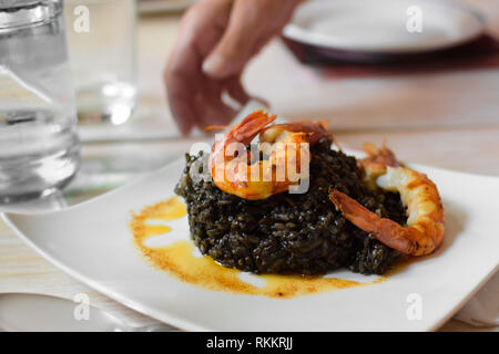 Paella aus schwarzem Reis mit Meeresfrüchten Garnele auf einem weißen Teller auf dem Tisch, Seitenansicht Stockfoto