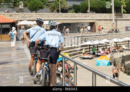 Beiden Beamtinnen von Cascais, patrouillieren Strandpromenade auf Fahrrädern. Menschen sind Sunburning auf dem öffentlichen Strand an der Atlantikküste. Stockfoto