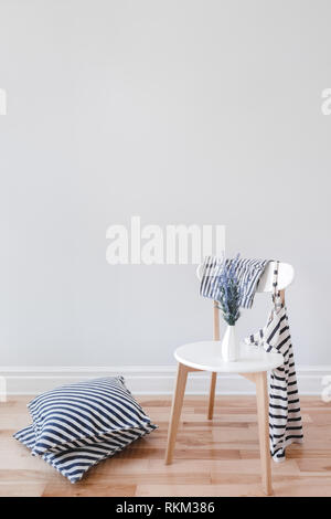 Moderne Einrichtung mit eleganten Stuhl, Lavendelblüten, gestreiften Polstern und Kleidung, auf grauen Hintergrund mit kopieren. Stockfoto