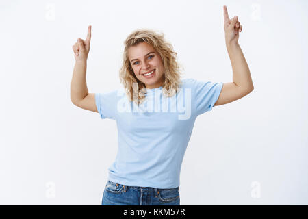 Verpassen Sie nicht die Chance und schauen Sie oben. Portrait von angenehmen und niedliche blonde europäische Frau mit blauen Augen und nettes Lächeln, Neigekopf freudig grinsend und Stockfoto