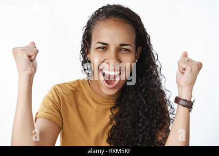 Glücklich und begeistert mich afrikanische amerikanische Mädchen mit lockigem Haar die geballten Fäuste in Beifall und Erfolg schreien Ja und freudig Schielen Stockfoto