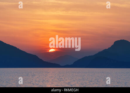 Schönen Sonnenuntergang an der Küste. Sonne hinter dem Stein und Sonnenlicht weg über das Wasser. Stockfoto