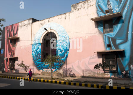 Frau geht hinter einem großen Wandgemälde an der Seite des Gebäudes in Lodhi Kolonie, New Delhi, Indien gemalt Stockfoto