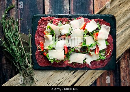 Frisches Rindfleisch Carpaccio mit Rasierte Parmesan, Chili und Rucola auf einem flachen Lay-Foto Stockfoto