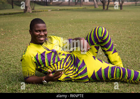 Afrikanische Mann im offenen Bereich der grünen Gras, klarer Himmel präsentiert imaginären Produkt oder Service mit guten Nachrichten vom Telefon ab. Stockfoto