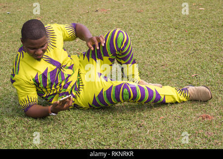 Afrikanische Mann im offenen Bereich der grünen Gras, klarer Himmel präsentiert imaginären Produkt oder Service mit guten Nachrichten vom Telefon ab. Stockfoto