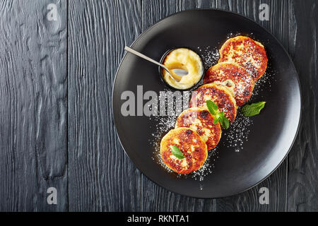 Deutsche quark Kartoffelpuffer - Quarkkeulchen mit Puderzucker bestreut und mit Minze auf einer schwarzen Platte mit Apple Mousse eingerichtet, f Stockfoto