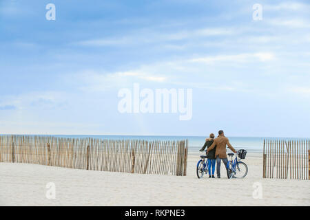 Paar Reiten Fahrräder auf den Strand von Le Touquet im Winter. Paar gesehen von hinten mit Blick auf das Meer und ganivelles, Zäune zu stabilisieren. Stockfoto