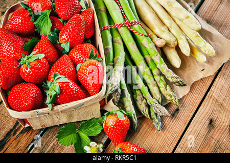 Box von frischem saftigen roten Erdbeeren und Bündel von weißem und grünem Spargel Spears auf einem rustikalen Holztisch in der Nähe zu sehen, von oben Stockfoto