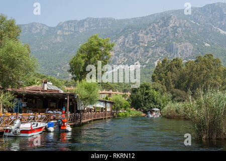 Akyaka, Mugla, Türkei - 30. Juli 2016. Azmak stream in Akyaka Dorf in der Provinz Mugla in der Türkei, mit Restaurant, Boote und Sakar Berge in der b Stockfoto