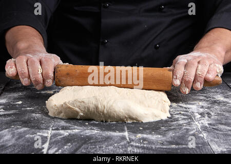 Koch in einem schwarze Tunika, rollt Teig für Pizza, in der Nähe Stockfoto