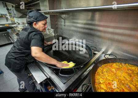 Ein Koch reinigt ein großer schwarzer Topf beim Kochen Paella im Restaurant Küche in Valencia, Spanien. Stockfoto