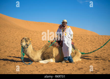 Merzouga, Marokko - Januar 13, 2019: Berber Mann mit seinem Kamel warten auf Touristen in der Sahara Stockfoto