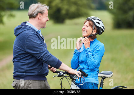 Active Senior Frau setzt auf einem Fahrrad Helm mit Partner vor der Fahrt mit dem Fahrrad Stockfoto