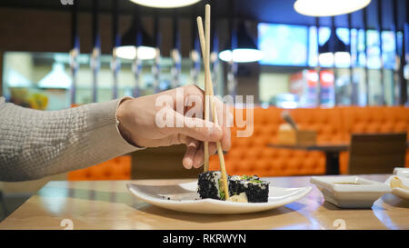 Junger Mann mit Stäbchen nimmt Sushi aus einer Platte in ein japanisches Restaurant. Männer startet frisst der japanischen Küche. Stockfoto