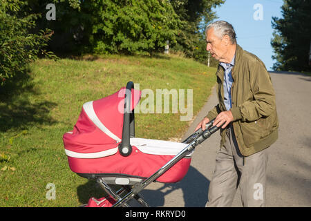 Großvater trägt Enkelin in Rosa Baby carriager bei Sonnenuntergang. Outdoor im Land. Stockfoto