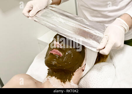 Kosmetikerin Arbeitnehmer setzt Alufolie auf weibliche Kunden Gesicht, Verfahren nach dem Anwenden kosmetische Gesichtsmaske von Meer ​​Algae Stockfoto