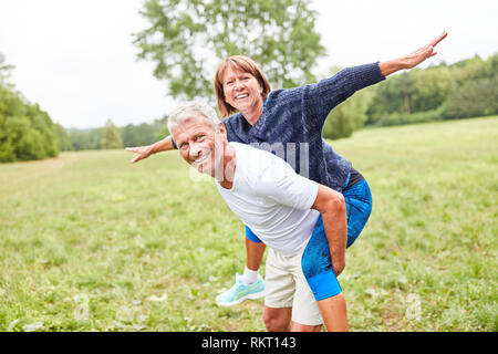 Ältere Frau reitet Huckepack auf ihrem Partner zurück in den Park im Sommer Stockfoto