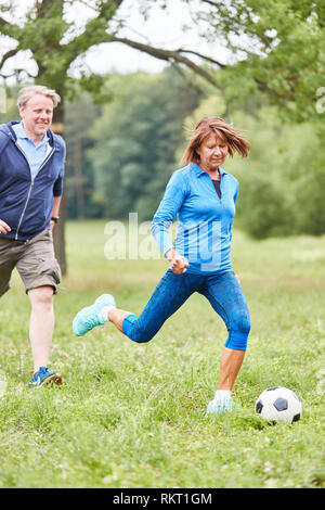 Ältere Frau Fußball spielen mit Freunden im Park als Senior Sport Stockfoto