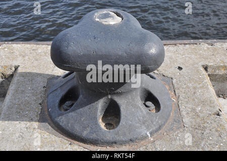 Gusseisen Kai Poller gegen Hell rusty Beton- und dunklen Wasser Wellen. Stockfoto