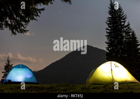 Zwei hell leuchtende, touristische Zelte auf der grünen Wiese Wald Lichtung auf dunklen Berg und dem klaren, blauen Sternenhimmel Kopie Raum Hintergrund. Tourismus, Nacht campin Stockfoto
