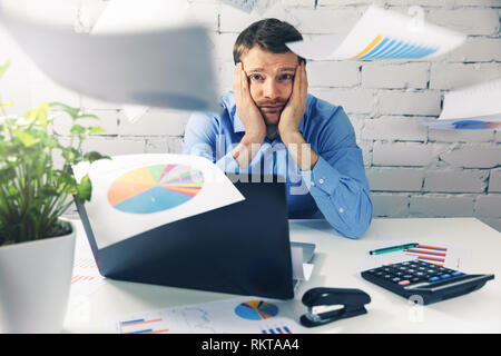 Erschöpft im Büro sitzen am Schreibtisch mit fliegenden Diagramm und Tabelle Papiere um Stockfoto