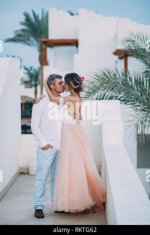 Glückliche Brautpaar Kuss auf der Terrasse des weißen Villa gegen den Hintergrund der Palmen Niederlassungen während der Flitterwochen in Ägypten. Stockfoto